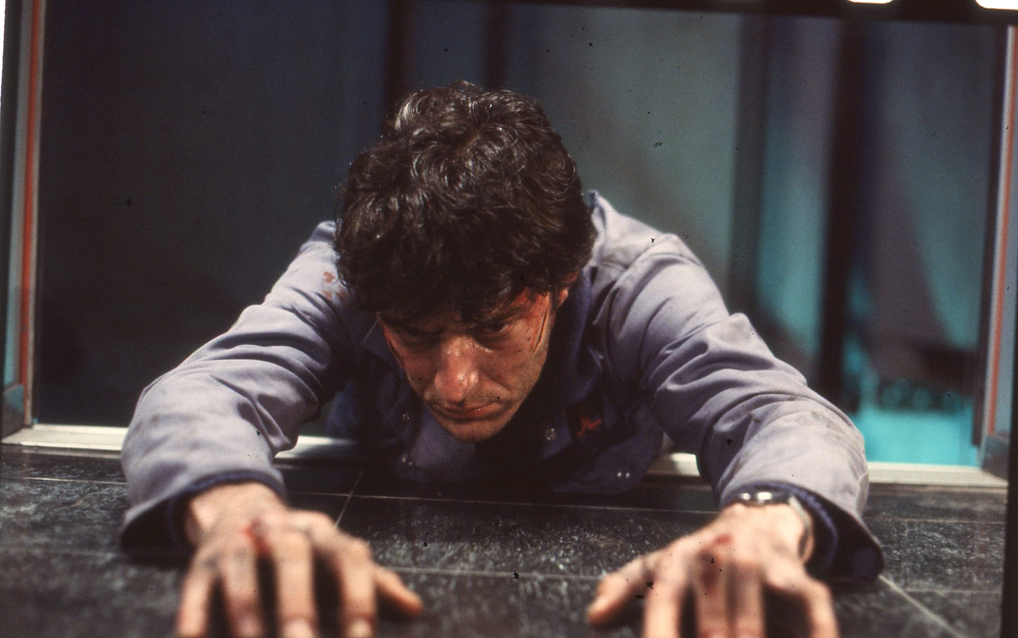 Afbeelding van een man die moeite heeft om uit een open liftschacht te kruipen. Uit de film De lift.