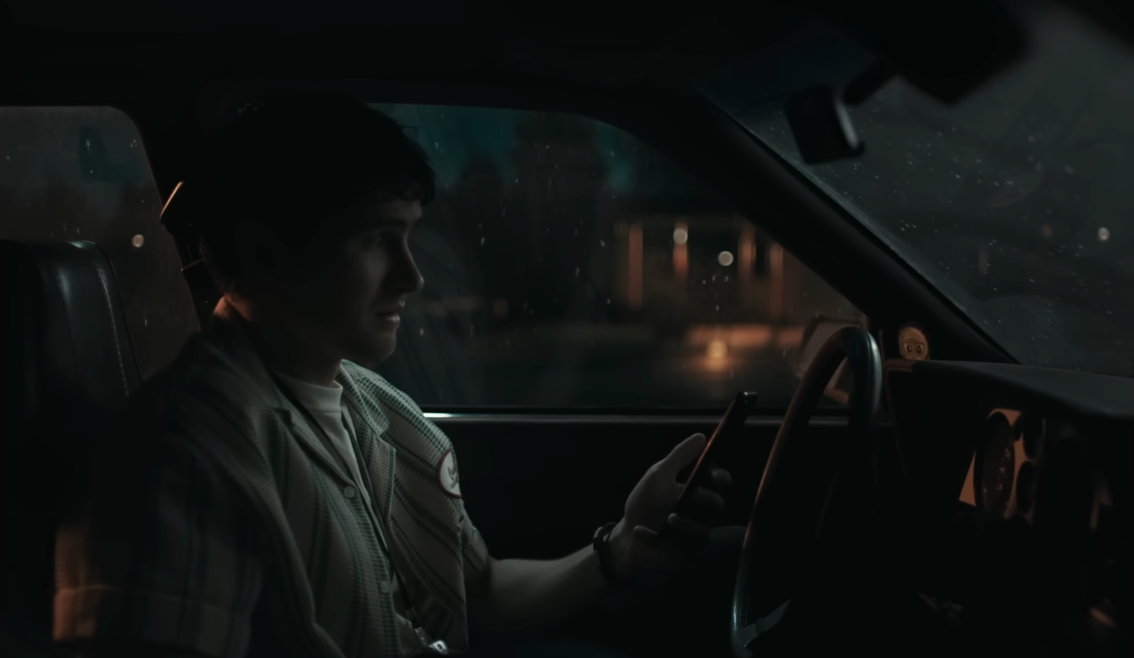 Een afbeelding van een jonge jongen die in zijn auto die geparkeerd staat aan het bellen is, in de nacht.