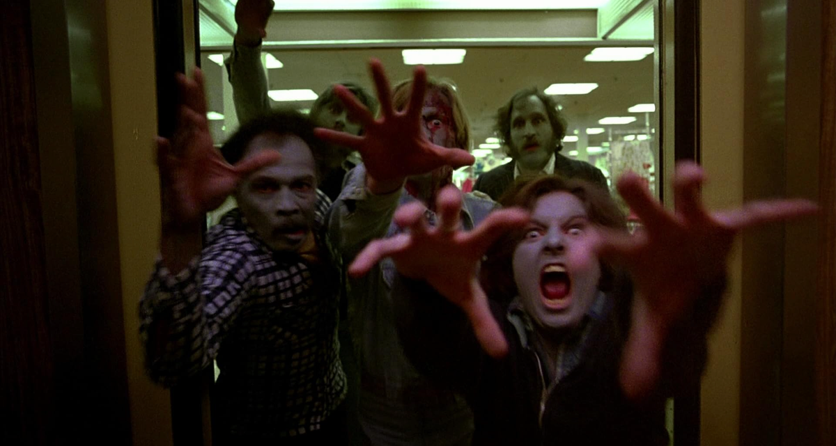 Afbeelding met naar de camera grijpende zombies.