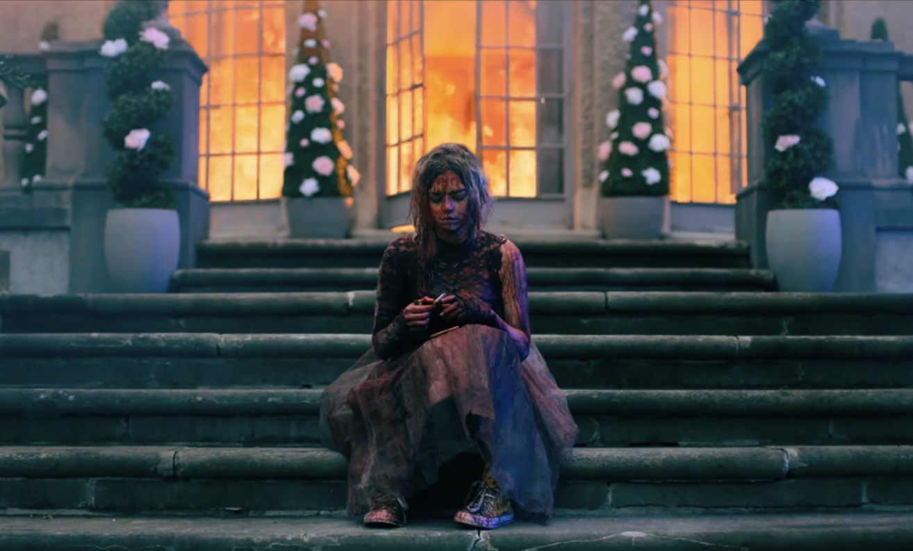 Een afbeelding van een bebloede vrouw op een trap met achter haar een brandend huis.