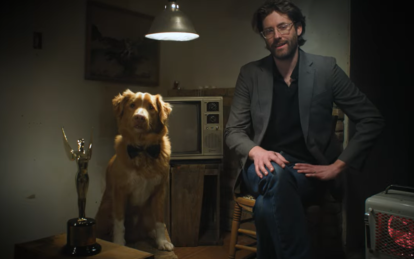Een afbeelding van een man op een stoel, en een hond op een kruk. De hond heeft een filmprijs ontvangen voor de rol in Good Boy.