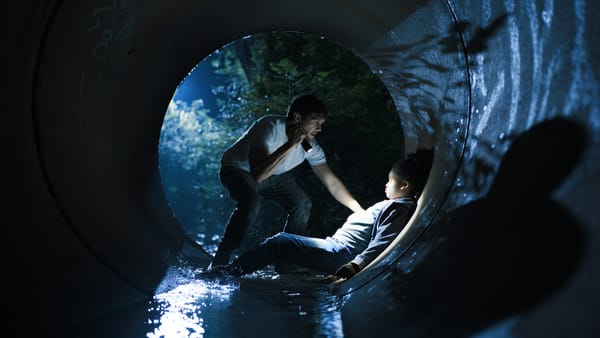 Een afbeelding van een man met zaklamp die schijnt om een meisje, in een grote afwateringsbuis