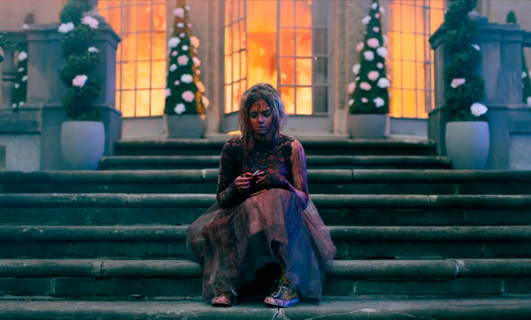 Een afbeelding van een bebloede vrouw op een trap met achter haar een brandend huis.